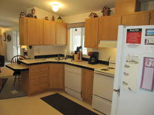 Kitchen featuring lofted ceiling, natural light, electric range oven, refrigerator, dishwasher, range hood, light floors, and brown cabinetry