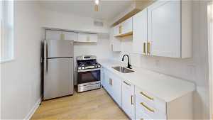 Unit 10 Kitchen featuring refrigerator, gas range oven, light parquet floors, white cabinets, and light countertops