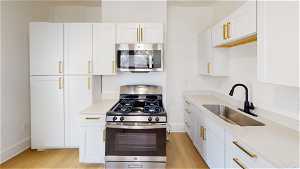 Unit 1 Kitchen with gas range oven, microwave, white cabinetry, light countertops, and light hardwood flooring