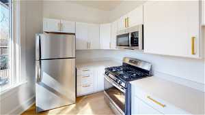 Unit 2 Kitchen with gas range oven, microwave, refrigerator, light countertops, white cabinets, and light hardwood flooring