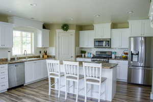 Kitchen with a kitchen breakfast bar, hardwood floors, natural light, gas range oven, refrigerator, dishwasher, microwave, dark granite-like countertops, and white cabinets