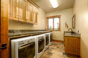 Washroom featuring cabinet space, a sink, stone finish floor, baseboards, and washer and clothes dryer