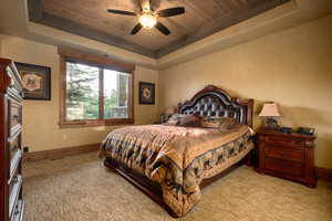 Bedroom featuring light carpet, baseboards, ceiling fan, a raised ceiling, and wood ceiling
