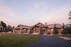 View of front of property featuring a lawn, curved driveway, a chimney, and stone siding