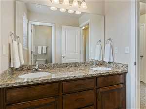 Half bathroom with mirror, toilet, and dual bowl vanity
