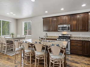 Kitchen featuring a kitchen breakfast bar, natural light, hardwood flooring, gas range oven, microwave, granite-like countertops, and dark brown cabinetry