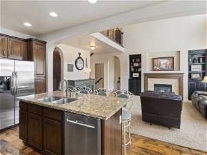 Kitchen with a fireplace, refrigerator, dishwasher, light hardwood flooring, kitchen island sink, and dark brown cabinetry