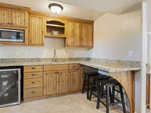 Kitchen featuring a kitchen bar, microwave, light floors, brown cabinets, and light granite countertops