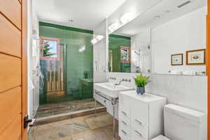 Full bathroom featuring mirror, toilet, shower booth, and vanity with extensive cabinet space