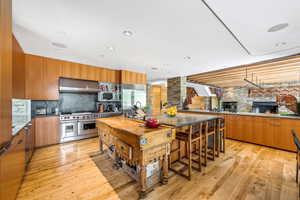 Kitchen featuring a kitchen bar, a kitchen island, extractor fan, gas range oven, refrigerator, light hardwood floors, and brown cabinetry