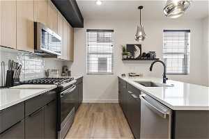 Kitchen featuring natural light, microwave, gas range oven, stainless steel dishwasher, light parquet floors, light countertops, and pendant lighting