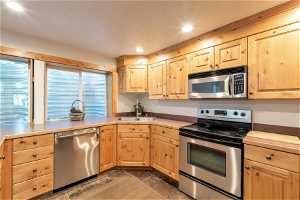Basement Apartment Kitchen featuring microwave, electric range oven, stainless steel dishwasher, brown cabinets, and light countertops