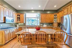 Kitchen with a breakfast bar, natural light, microwave, refrigerator, gas cooktop, light stone countertops, light parquet floors, and brown cabinets