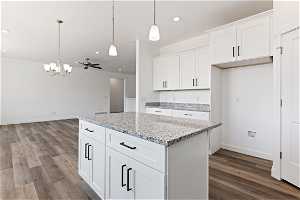 Kitchen with wood-type flooring, light stone countertops, pendant lighting, and white cabinetry