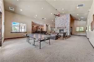 Playroom with ceiling fan, a high ceiling, plenty of natural light, a fireplace, vaulted ceiling, and light carpet
