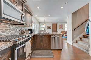 Kitchen with backsplash, pendant lighting, light stone countertops, light hardwood flooring, and appliances with stainless steel finishes