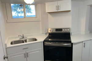 Kitchen with stainless steel electric range, light countertops, and white cabinets