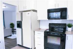 Kitchen featuring light hardwood floors, light countertops, backsplash, white refrigerator with ice dispenser, and electric range
