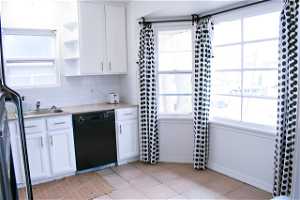 Kitchen featuring white cabinets, backsplash, light tile floors, light countertops, and black dishwasher