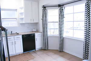 Kitchen featuring white cabinets, backsplash, light tile floors, light countertops, and black dishwasher