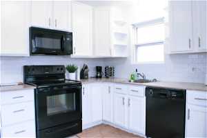 Kitchen featuring light countertops, backsplash, black appliances, light tile floors, and white cabinetry