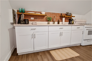 Kitchen with white cabinets, backsplash, range, hardwood flooring, and light countertops