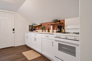 Kitchen with light countertops, backsplash, range with gas stovetop, wood-type flooring, lofted ceiling, and white cabinetry