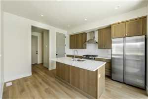 Kitchen with high end refrigerator, light lvp floors, light countertops, wall chimney range hood, and backsplash