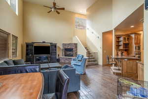 Living room with ceiling fan, a fireplace, a high ceiling, light hardwood flooring, TV, plenty of natural light, and lofted ceiling