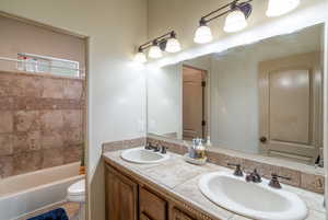 Full bathroom with double sink vanity, light tile floors, tiled shower / bath combo, and mirror