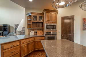 Kitchen featuring dark granite-like countertops, dark parquet floors, brown cabinets, and appliances with stainless steel finishes