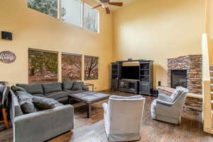 Hardwood floored living room featuring a high ceiling, a fireplace, ceiling fan, and TV