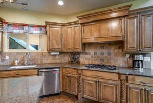 Kitchen with backsplash, premium range hood, dark stone counters, brown cabinets, and stainless steel appliances