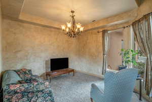 Carpeted living room featuring a tray ceiling, a chandelier, and TV