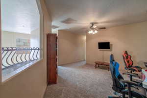 Office area with a textured ceiling, ceiling fan, TV, and light carpet