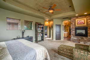 Bedroom with ceiling fan, a tray ceiling, carpet, and a fireplace