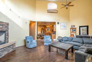 Living room with ceiling fan, a high ceiling, a fireplace, vaulted ceiling, and dark hardwood floors