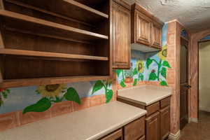 Kitchen featuring a textured ceiling, tile floors, brown cabinets, and light countertops