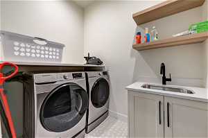 Clothes washing area featuring washer and clothes dryer, cabinets, sink, and light tile floors