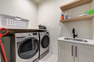 Clothes washing area featuring washer and clothes dryer, cabinets, sink, and light tile floors