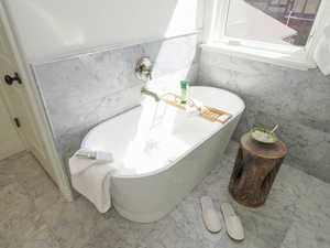 Bathroom featuring a bath, tile walls, and light tile flooring