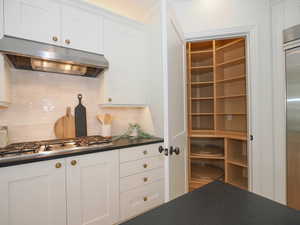 Kitchen featuring stainless steel gas stovetop, backsplash, white cabinetry, and dark countertops