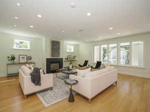 Hardwood floored living room featuring a fireplace, ornamental molding, and plenty of natural light