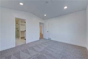 Unfurnished bedroom featuring a walk in closet, light carpet, ensuite bath, and vaulted ceiling