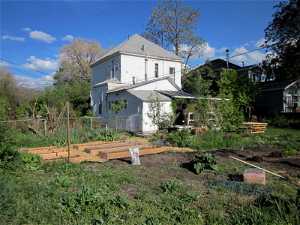 Wide view of back yard and rear elevation of the house with various gardening activities.