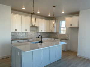 Kitchen featuring white cabinetry, a kitchen island with sink, pendant lighting, hardwood floors, light countertops, and backsplash