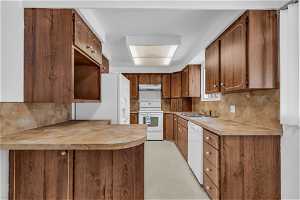 Kitchen with brown cabinets, light tile floors, range, white dishwasher, light countertops, and backsplash