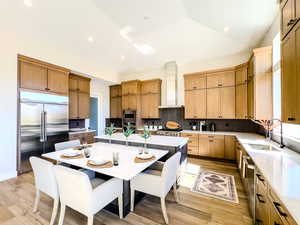 Kitchen with vaulted ceiling, a kitchen island, built in appliances, sink, and wall chimney range hood