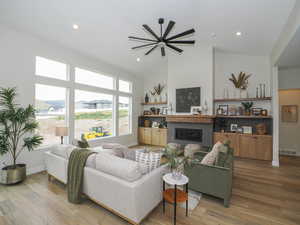 Living room with light hardwood flooring, lofted ceiling, ceiling fan, a fireplace, and a high ceiling