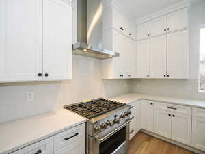 Kitchen with white cabinets, light hardwood / wood-style floors, wall chimney range hood, and stainless steel range